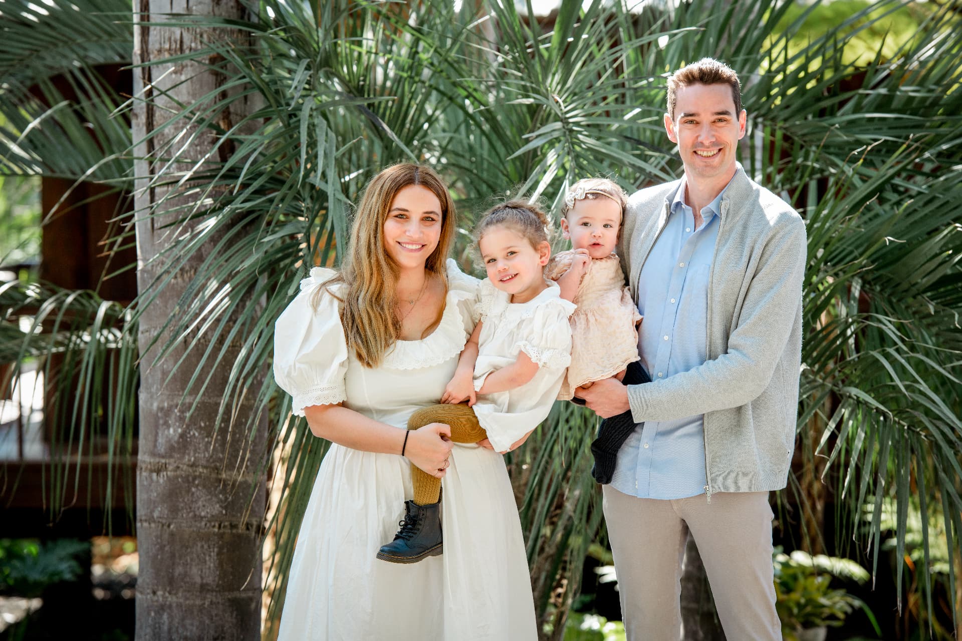 Family of four in cream and light blue standing beneath palm fronds