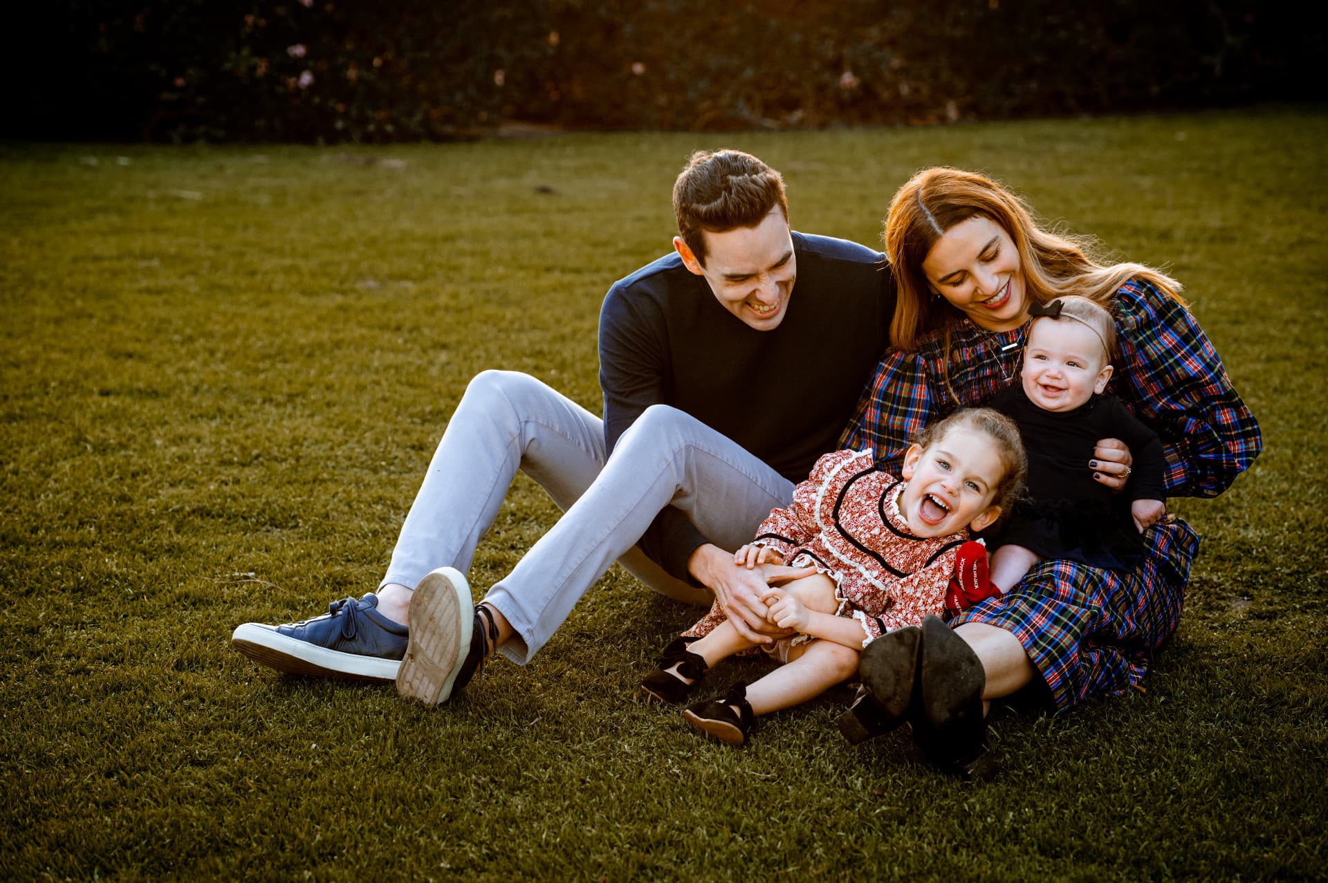 Family of four laughing on the grass in plaid and floral prints