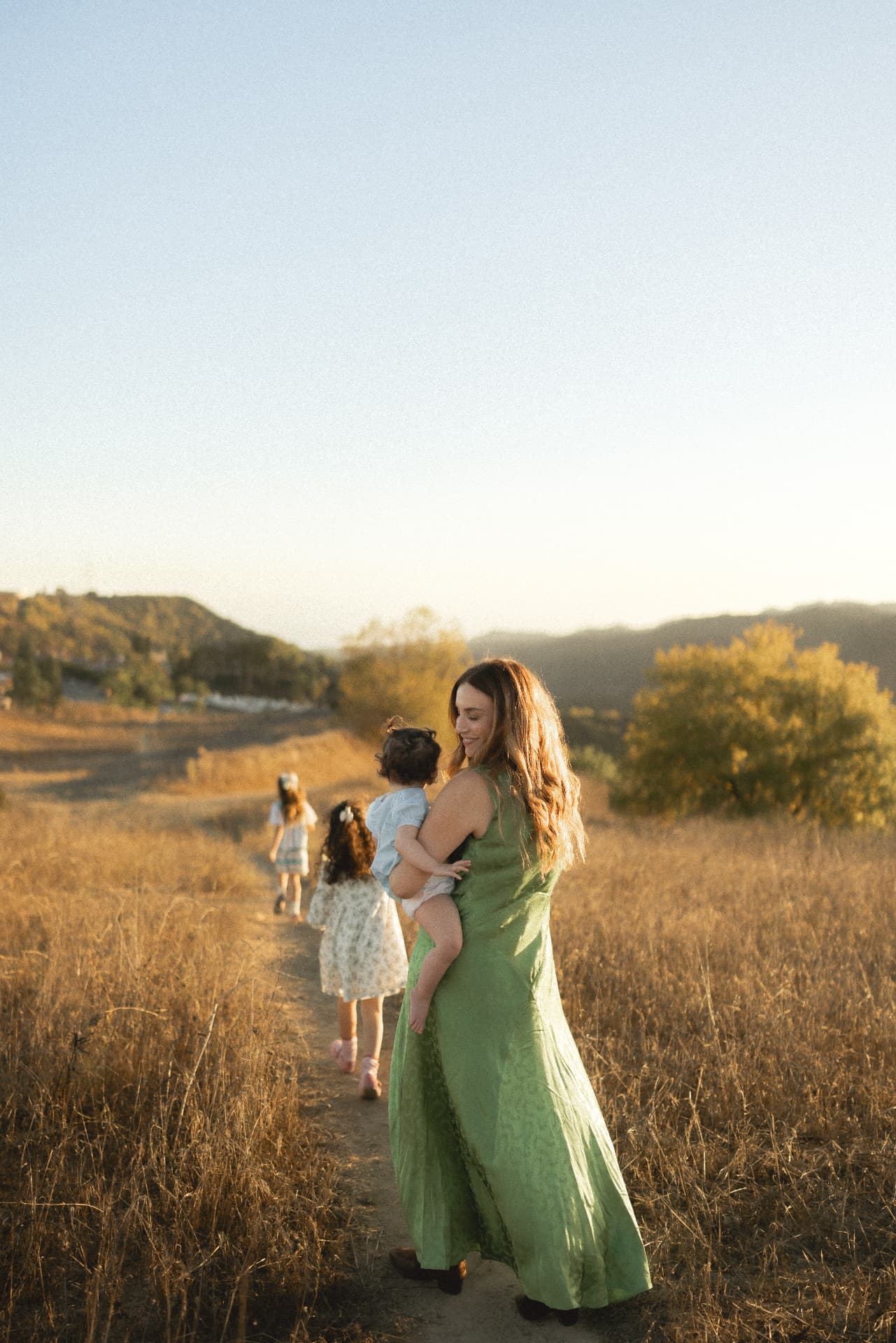 Mother in a green dress walking a trail with her children