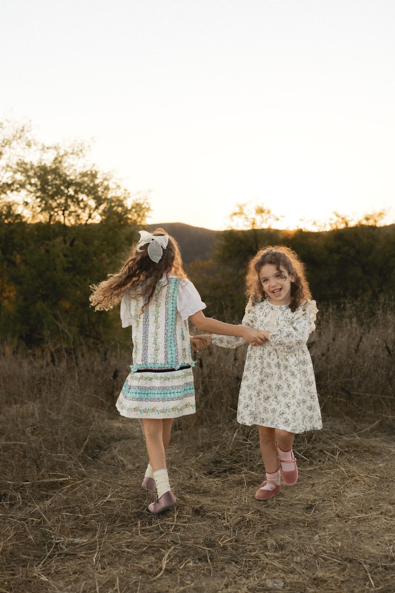 Two sisters holding hands and dancing in a golden field at sunset