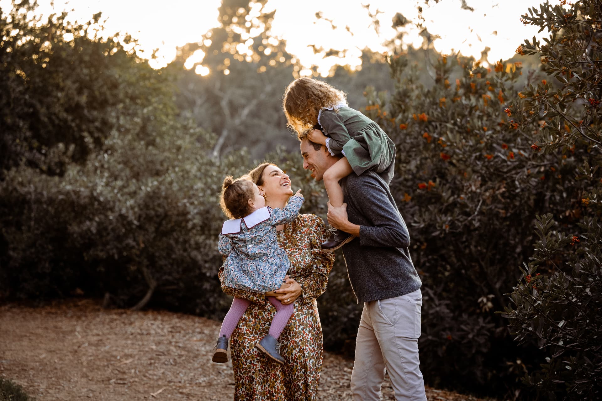 Family of four laughing together at golden hour, dad carrying his daughter on his shoulders