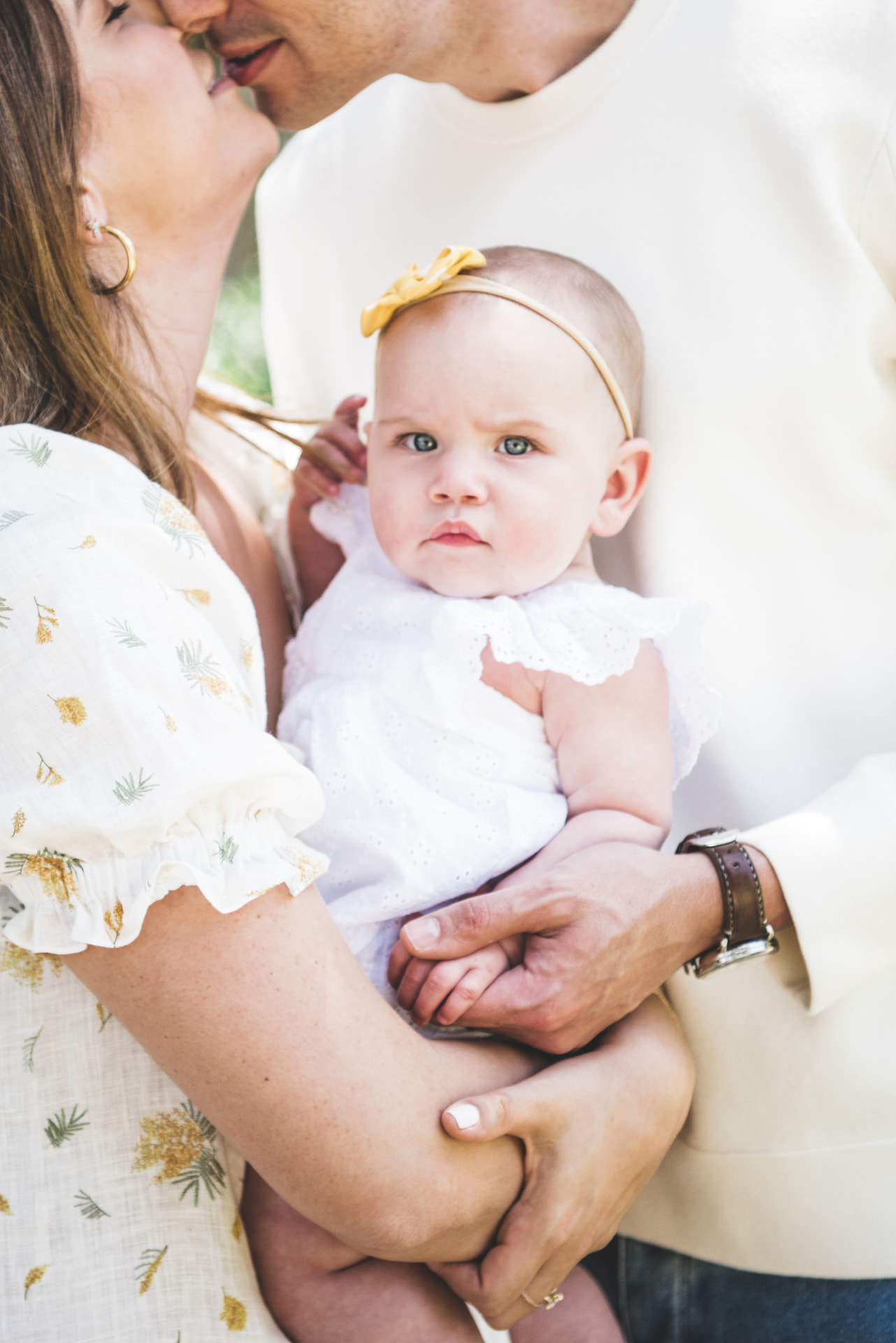 Parents holding their baby in a white eyelet dress
