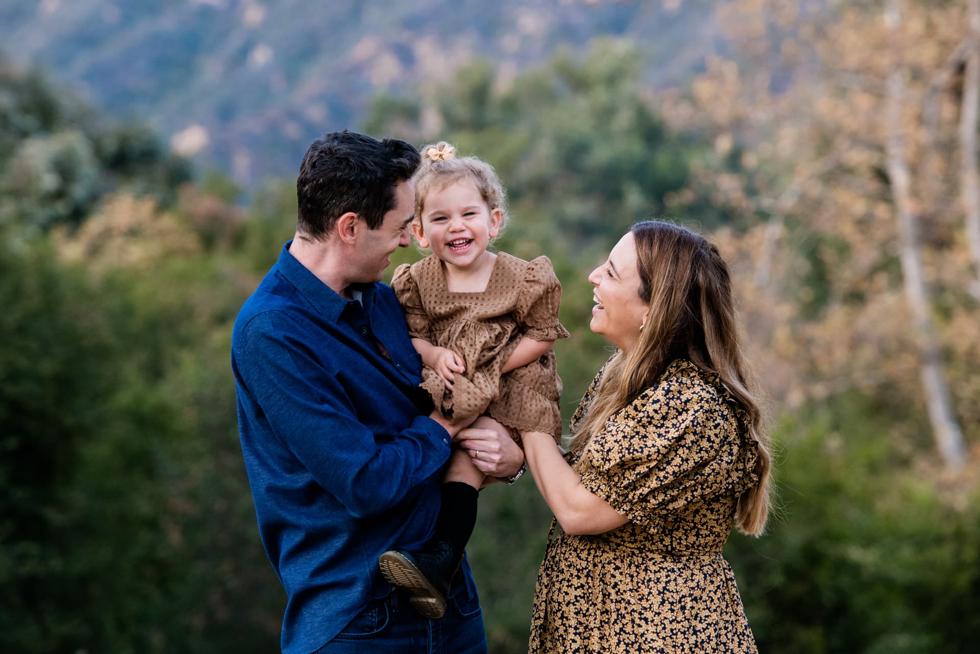 Parents laughing with their toddler in a brown eyelet dress