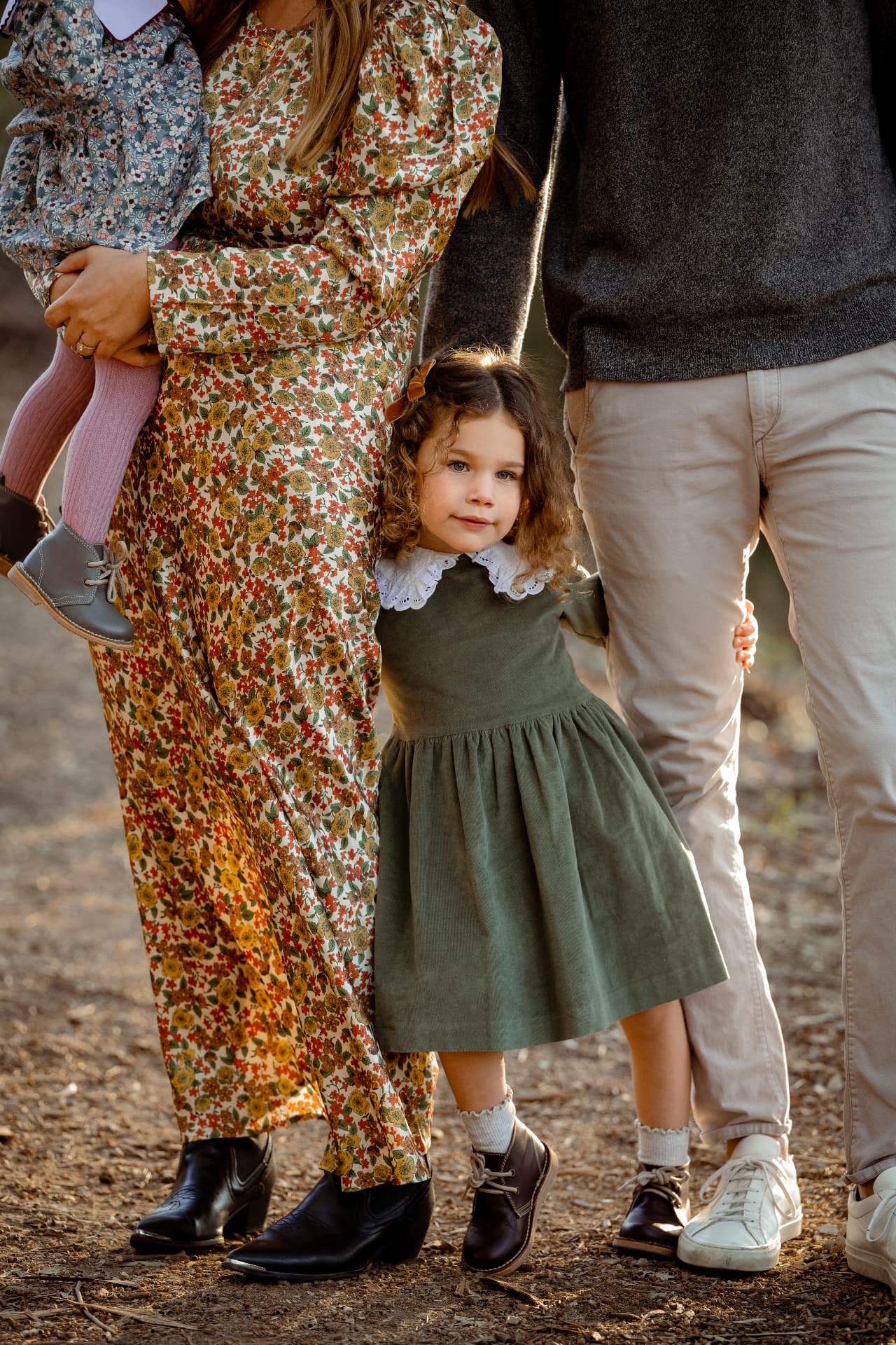 Detail of a girl in a green corduroy dress standing between her parents